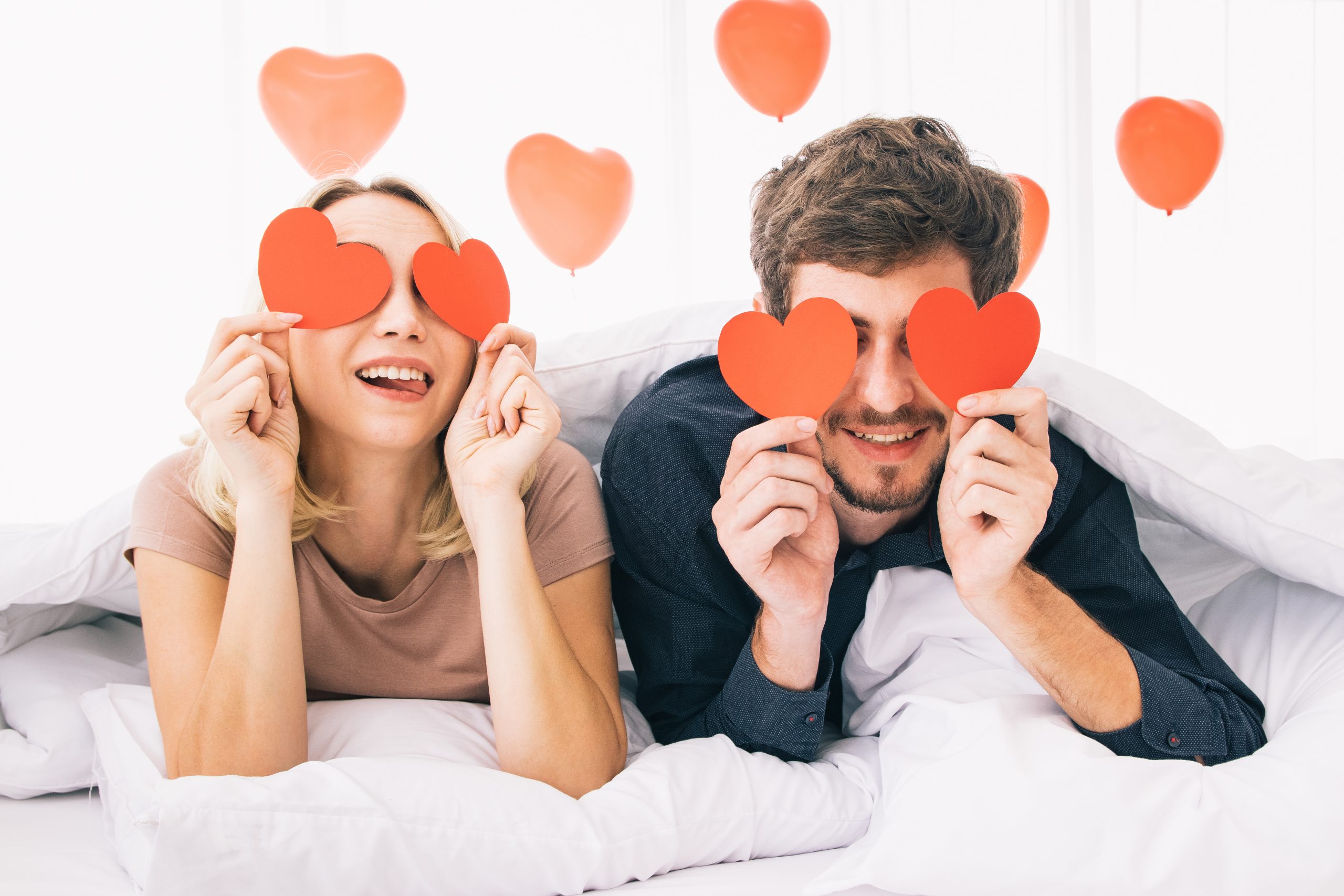 ベッドで仲良くハートに型紙を持ってるカップルの写真